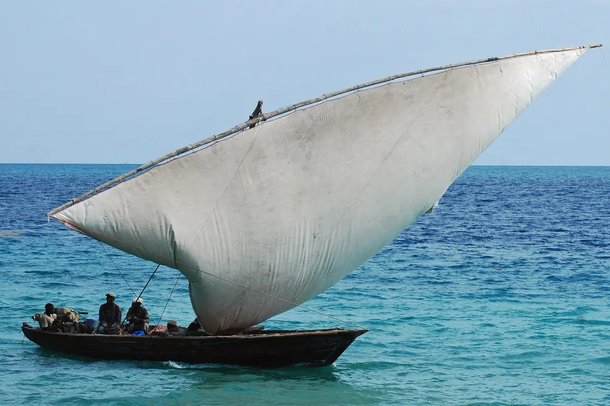 Wooden dhow with a large pale sail on bright turquoise sea