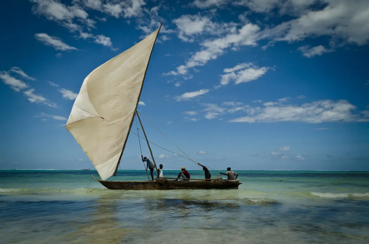 Traditionelles Dhau mit weißem Segel auf flachem blauem Wasser vor Sansibar